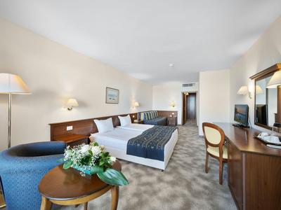 Modern hotel room with large bed, seating area, and desk.