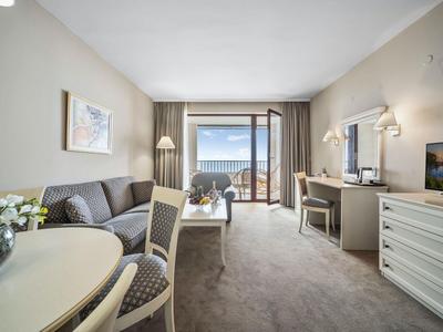 Chambre d'hôtel lumineuse avec canapé, table, télévision et balcon avec vue sur la mer.