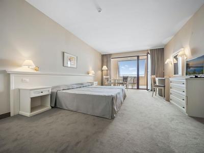 Chambre d'hôtel lumineuse avec lit, bureau, télévision et balcon offrant une vue sur la mer.