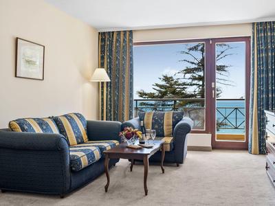 Cozy sitting area with sofa, armchair, small table, and balcony with sea view.