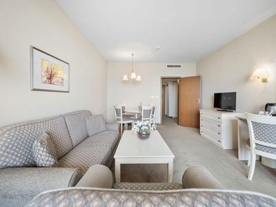 Chambre d'hôtel lumineuse avec canapé gris, table basse et table à manger en arrière-plan.