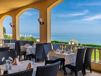 Terrace restaurant with set tables and sea view under blue sky.