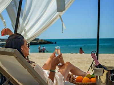 Personne se détend sur une chaise longue sous un auvent à la plage avec vue sur la mer et boissons.