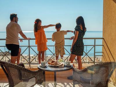 Famille debout sur balcon d'hôtel avec vue sur la mer par une journée ensoleillée.
