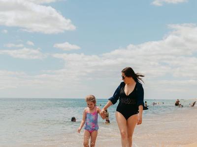 Femme et enfant marchant le long de la plage au bord de la mer sous un ciel nuageux.