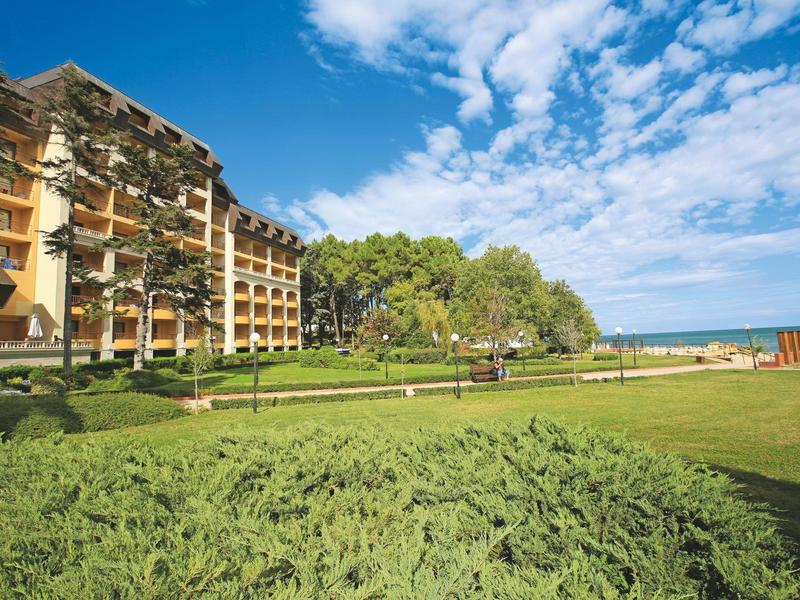 Hotel building next to a green lawn overlooking the sea under a blue sky.