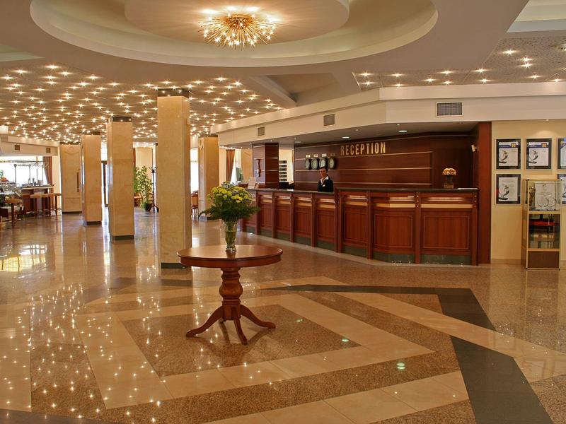 Large hotel lobby with shiny floor, reception desk, and decorative table in the center.