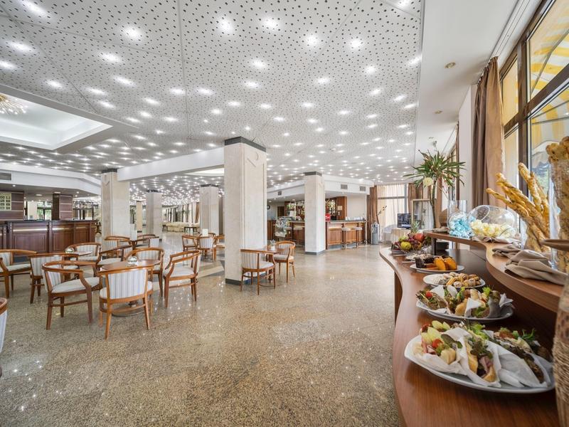 Large dining hall with set tables and a buffet featuring various dishes.
