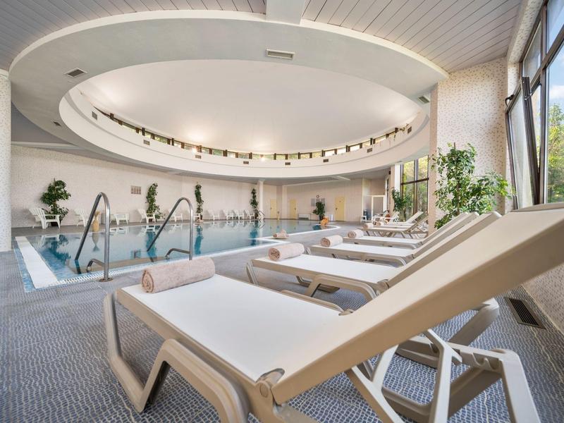 Bright indoor pool with lounge chairs and large windows overlooking trees.