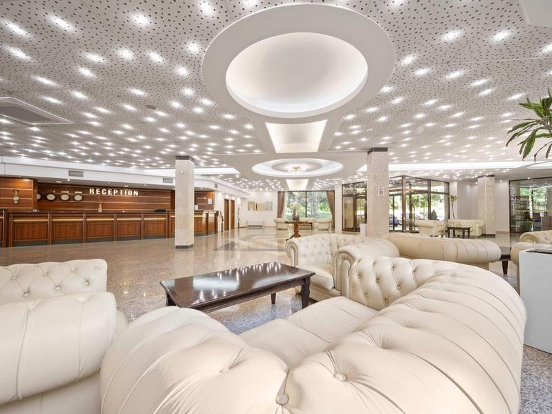 Elegant bright hotel lobby with white sofas and a ceiling adorned with lights.