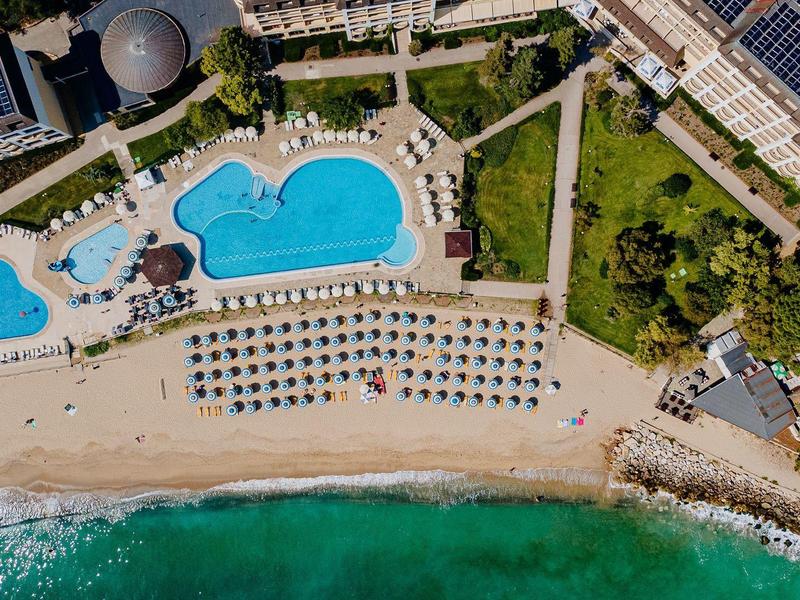 Aerial view of a resort with pools, beach loungers, and turquoise sea along the coast.