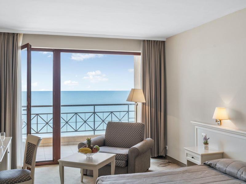Hotel room with sea view, balcony, armchairs, and warm lighting fixtures.