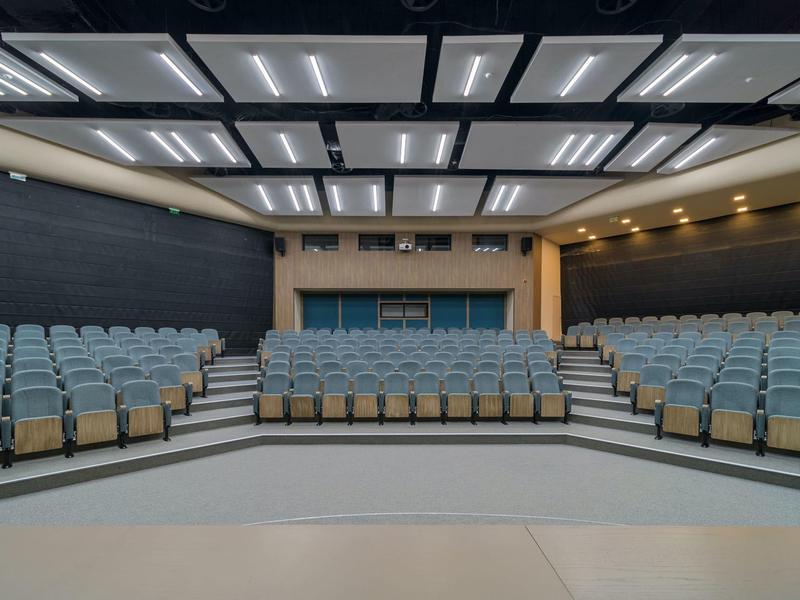 Modern auditorium with blue seating rows and bright ceiling lights.