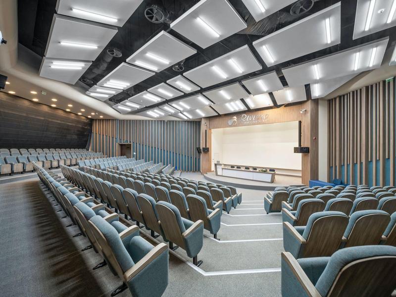 Modern large lecture hall with blue seating rows and bright stage.