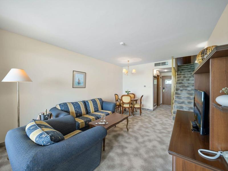 Living area with blue sofa, floor lamp, dining table, and TV in a cozy hotel room.