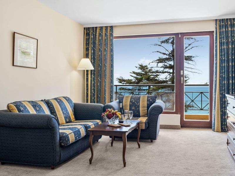 Cozy sitting area with sofa, armchair, small table, and balcony with sea view.