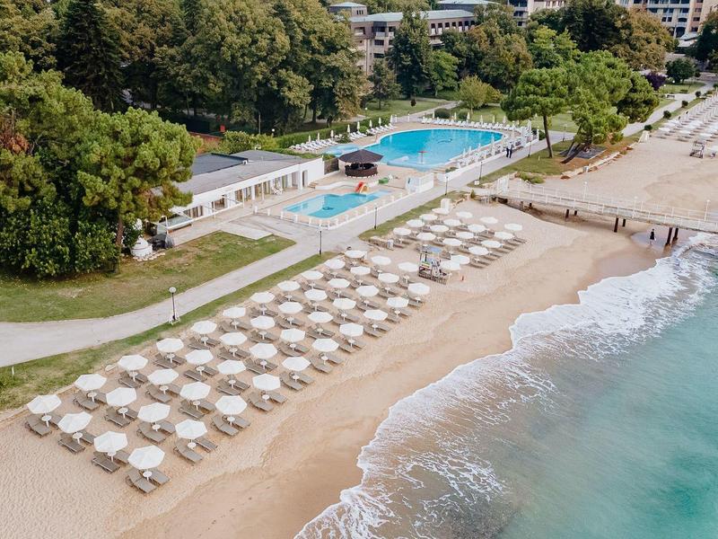 Beach with sun umbrellas, lounge chairs, and two pools next to hotel grounds.