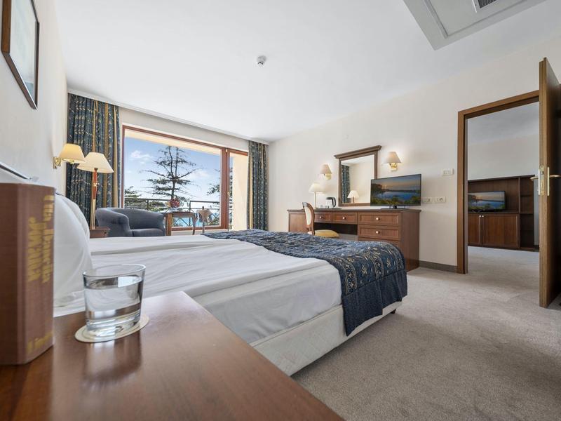 Bright hotel room with double bed, window overlooking an outdoor terrace, and wooden paneling.