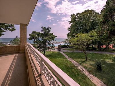 Balkon met metalen reling met uitzicht op een park en zee onder een bewolkte lucht