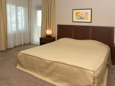 Slaapkamer met groot bed, nachtkastjes en gordijnen bij de ramen.