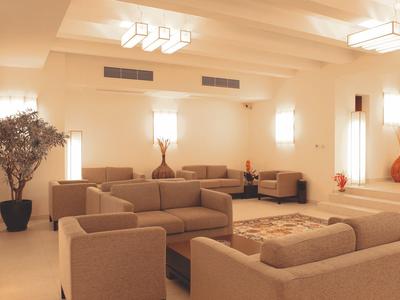 Lichte hotellobby met beige fauteuils, banken, tapijt en grote planten.