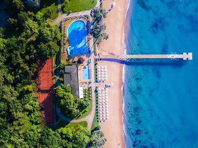 Luchtfoto van een strandresort met zwembad, ligstoelen en pier in de blauwe zee.