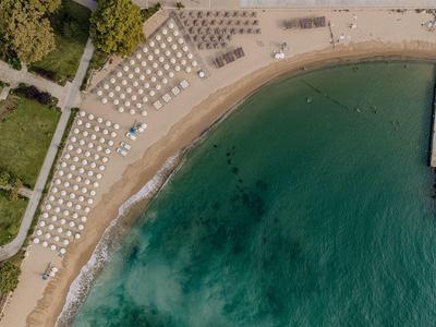 Luchtfoto van een zandstrand met ligstoelen naast de blauwe zee en een golfbreker.