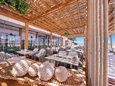 Overdekt terras met zitplaatsen en decoratieve kussens bij een hotelrestaurant.