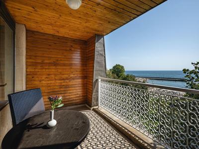 Balkon mit Holzwand, Tisch, Stuhl und Blick auf das Meer bei klarem Himmel.