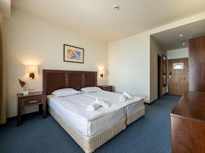 Lichte hotelkamer met twee bedden, nachtkastjes en houten kast.