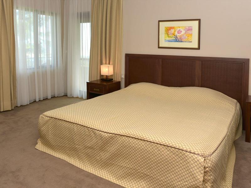 Slaapkamer met groot bed, nachtkastjes en gordijnen bij de ramen.