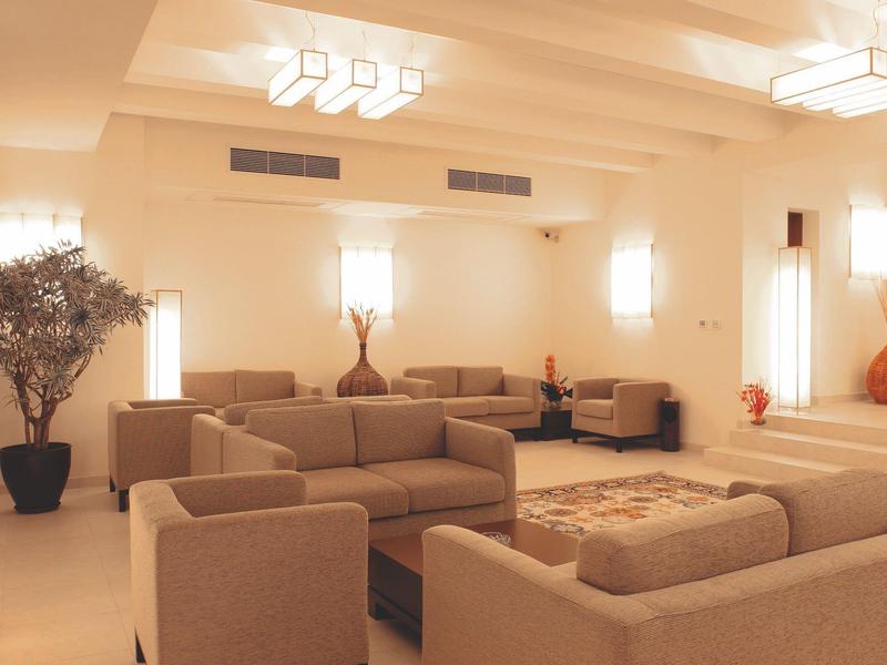 Helder, modern hotelwoonkamer met beige banken, tapijt en stijlvolle verlichting.