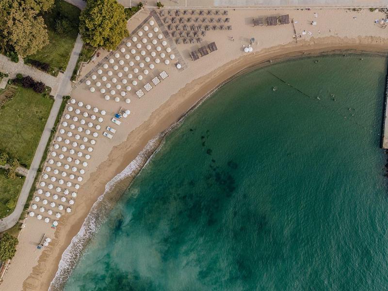 Luchtfoto van een zandstrand met ligstoelen naast de blauwe zee en een golfbreker.