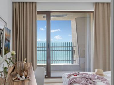 Světle zařízený hotelový pokoj s výhledem na moře skrz velká okna.