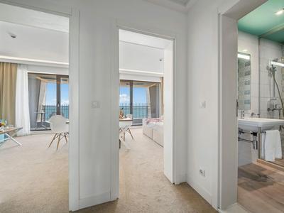 Světelná hotelová chodba s výhledem do dvou pokojů a koupelny se sprchou.