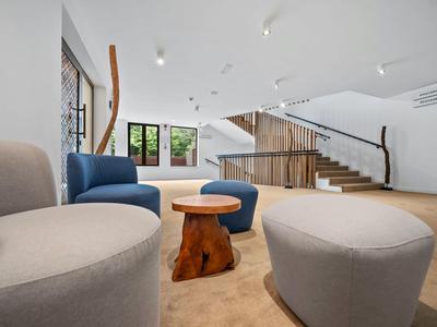 Moderní hotelová lounge s pohodlnými křesly, malým dřevěným stolkem a schodištěm v pozadí.