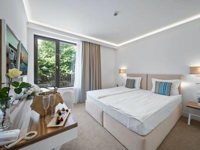 Moderní hotelový pokoj se dvěma jednolůžky, velkými okny a jednoduchou výzdobou.