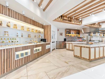 Moderní kavárna se světlým interiérem, dřevěnými panely a velkou výlohou nápojů a jídel.