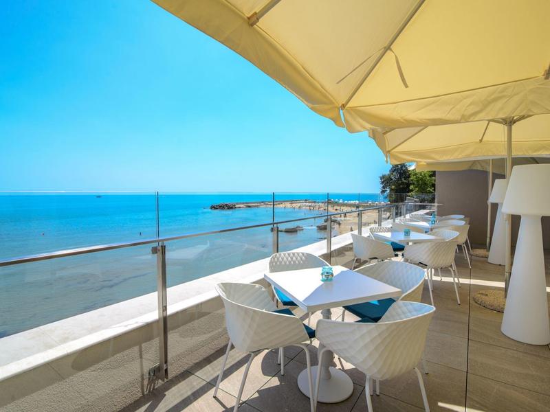 Terasa s bílými stoly a židlemi s výhledem na moře pod jasnou oblohou.