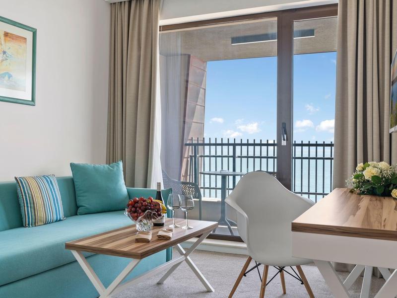 Moderně zařízený obývací pokoj s pohovkou, stolem a balkonem s výhledem na moře.