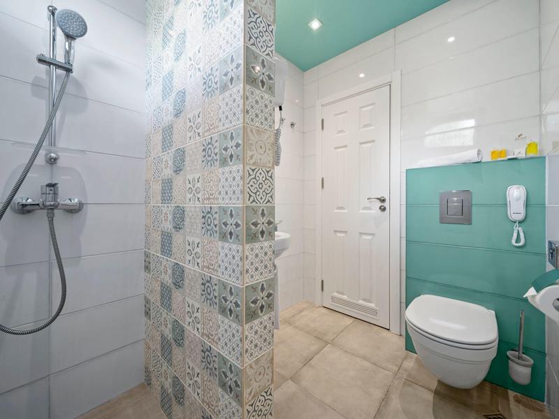 Moderní koupelna se sprchou, toaletou a tyrkysovými dlaždicemi na stěně.