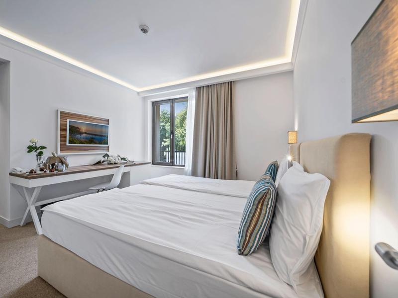 Moderní hotelový pokoj s velkou postelí, psacím stolem a přirozeným světlem z okna