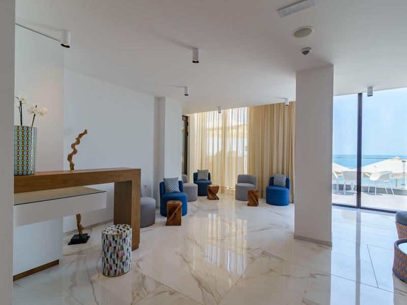 Moderní hotelový lounge s křesly, dřevěnou policí a výhledem na moře přes velká okna.