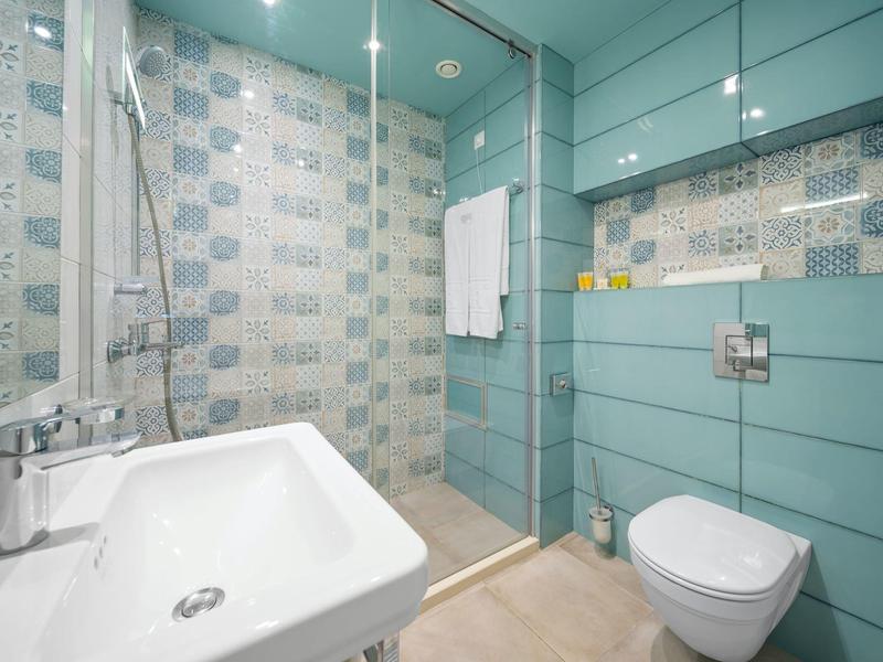 Moderní koupelna se sprchou, umyvadlem a toaletou, modrobílé obklady na stěnách.