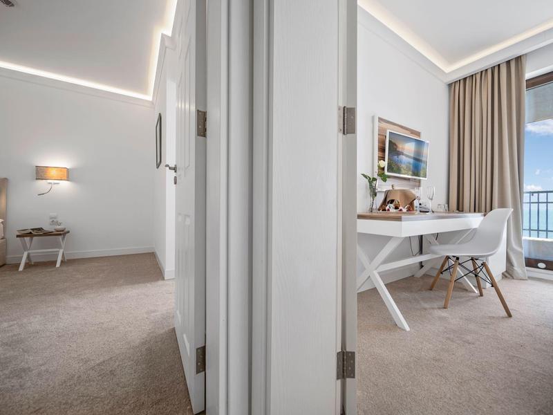 Výhled na moderní hotelový pokoj s samostatným pracovním koutem a balkonem s výhledem.