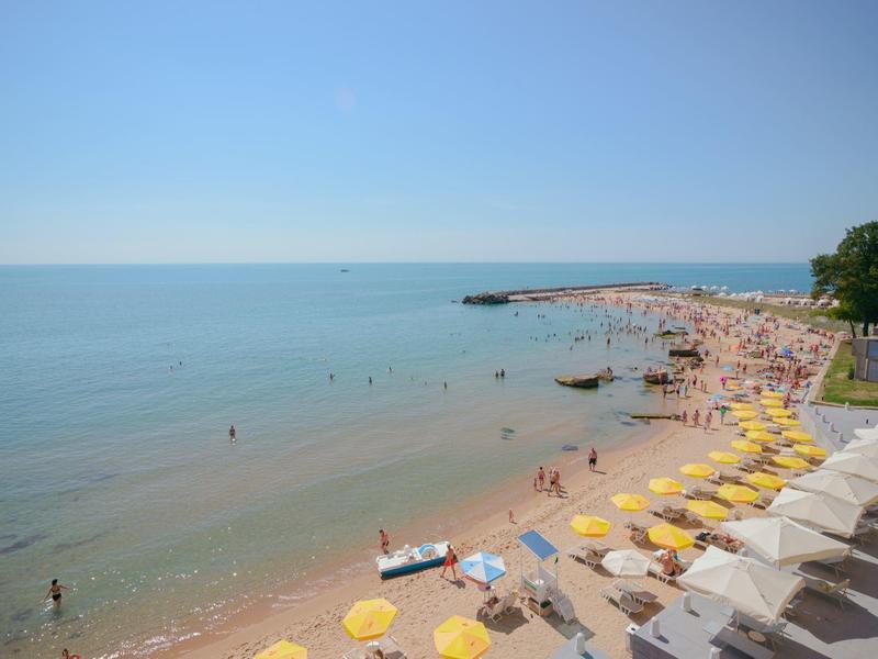 Pláž se žlutými slunečníky a lidmi u moře pod jasnou oblohou