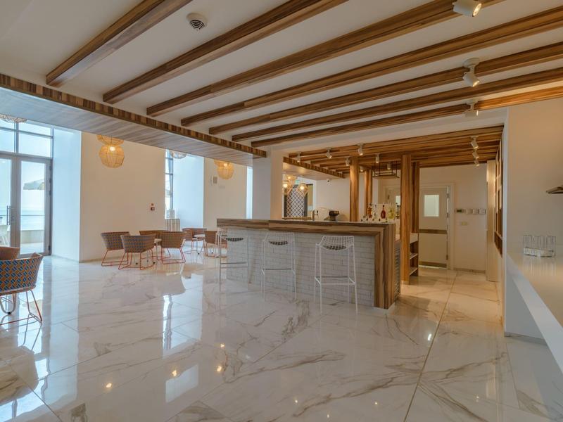 Moderní světlá hotelová jídelna s mramorovou podlahou, dřevěnými prvky a barovým posezením.