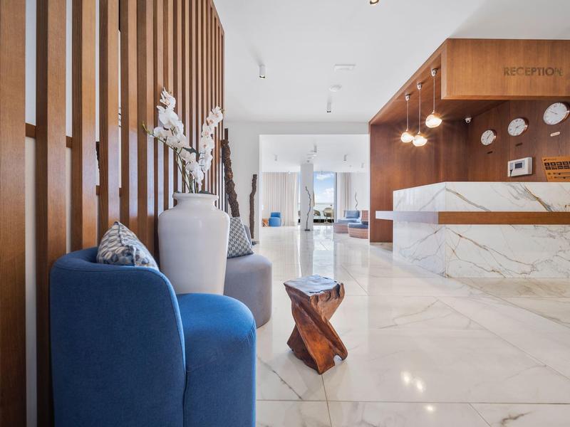 Moderní hotelová lobby s modrým křeslem, dřevěnou stěnou a mramorovou recepcí.