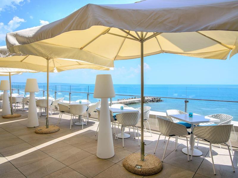 Terasa se slunečníky a stoly u moře za jasné oblohy