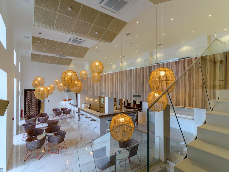 Moderní hotelová recepce s bílými stěnami, skleněnými zábradlími a teplým závěsným osvětlením.